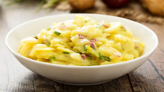 Für einen Kartoffelsalat kann man die Kartoffeln am Vortag kochen. Sie sind dann besonders gesund. | Fotolia.com, Martin Rettenberger Kartoffelsalat in einer weißen Schale angerichtet.