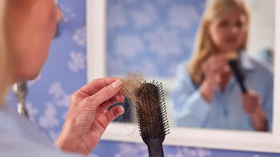 Eine Frau hält eine Bürste mit Haaren in der Hand.
