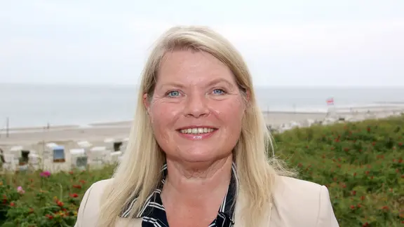 Eine blonde Frage lächelt und im Hintergrund sieht man das Meer.