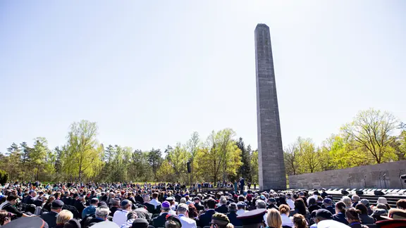 Besucher sitzen während einer Gedenkveranstaltung zum 80. Jahrestag der Befreiung des ehemaligen Konzentrationslagers Bergen-Belsen am Obelisken auf dem Gelände der Gedenkstätte Bergen-Belsen