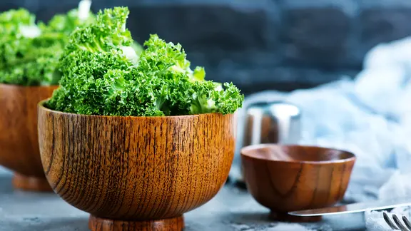 In den krausen Blättern versteckt sich häufig viel Sand. Frischen Grünkohl deshalb vor der Verarbeitung immer sorgfältig waschen. | Colourbox, Haivoronska_Y Frischer Grünkohl in einer Holzschale