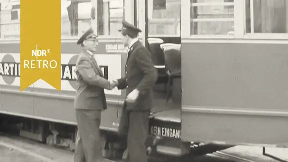 Schichtwechsel bei der Straßenbahn: Ein Fahrer in alter Uniform schüttelt einem Fahrer in neuer Uniform die Hand (1960)