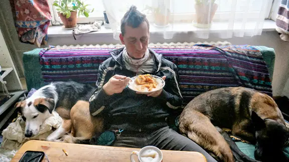 Der Ex-RAF-Terrorist Burkhard Garweg sitzt zwischen zwei Hunden auf einem Sofa.