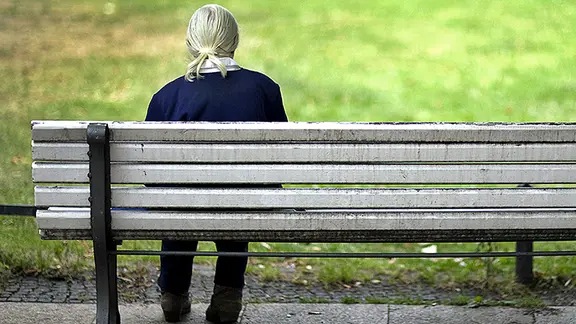 Eine alte Frau sitzt auf einer Parkbank.