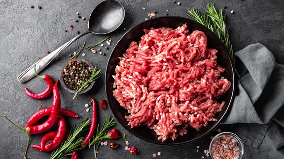 Eine Schüssel mit rohem Hackfleisch, daneben Gewürze.