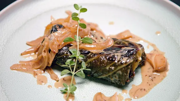 Vegetarische Wirsingroulade mit Zwiebelsoße auf einem Teller serviert
