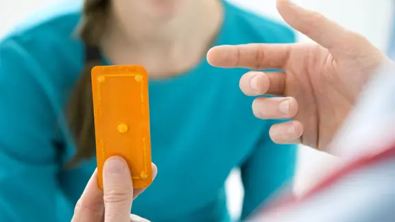 Hand eines Arztes hält bei Beratung einer Frau Blister mit Pille danach hoch
