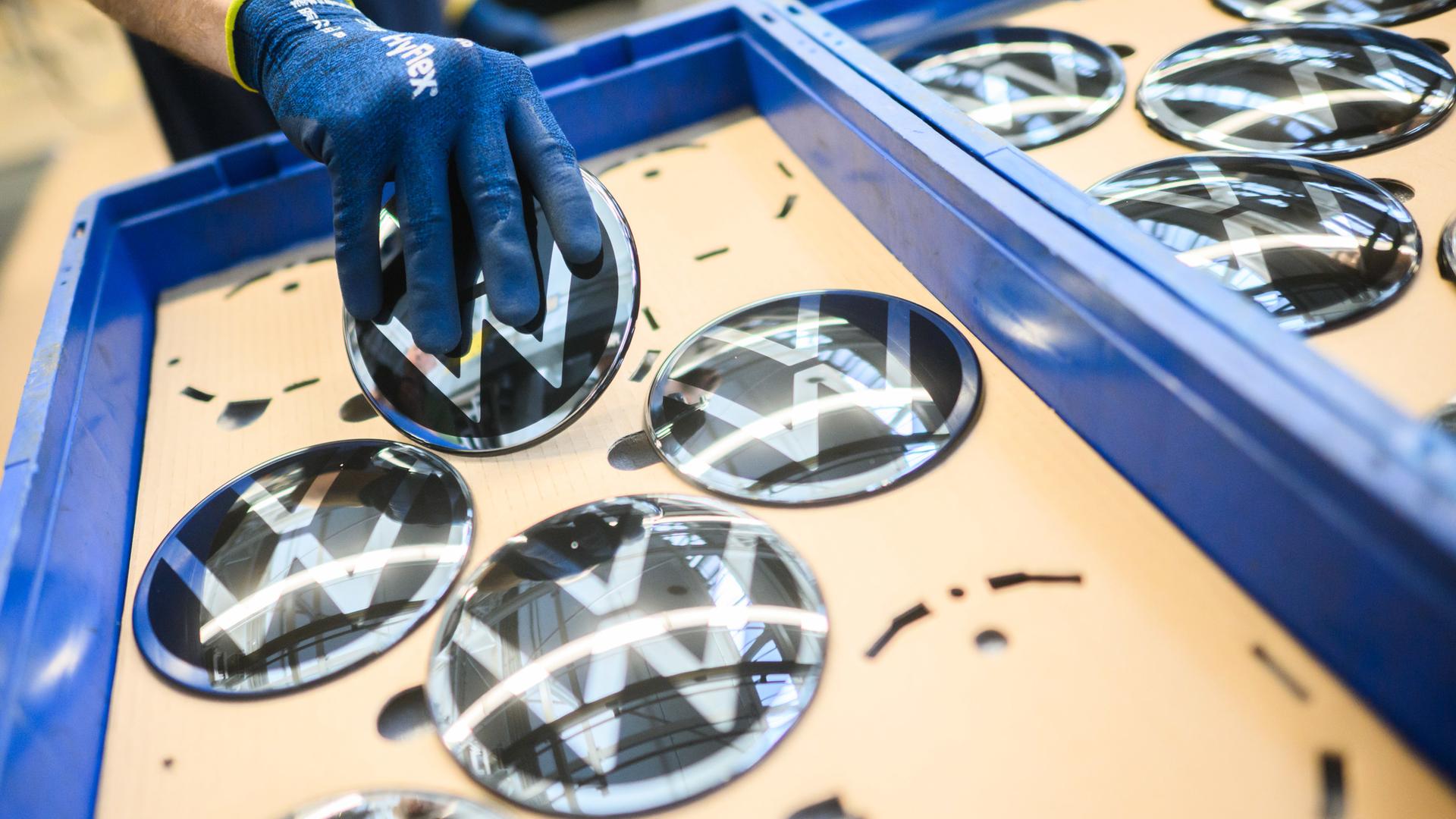 Ein Mitarbeiter hält im VW Stammwerk ein VW Logo für den Einbau in einen Neuwagen. | dpa-Bildfunk, Julian Stratenschulte