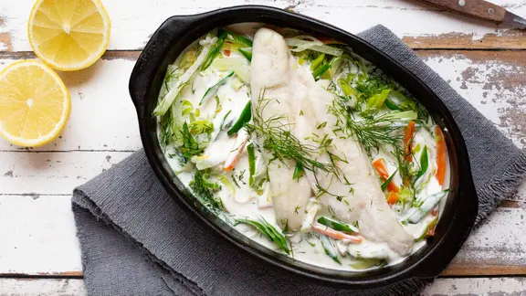 Fischpfanne mit Frühlingsgemüse in einem Bräter auf dem Tisch.