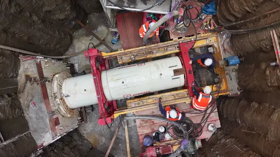 Drei Bauarbeiter arbeiten auf einer Baustelle an einer Röhre.