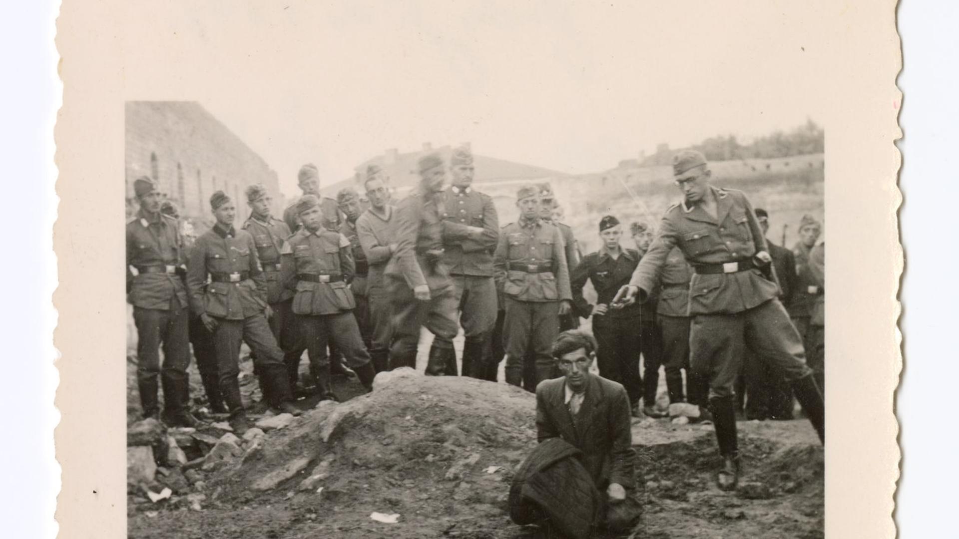 Auf einem alten Bild wird ein Mann von einem Soldaten mit einer Waffe bedroht. | Metropol-Verlag