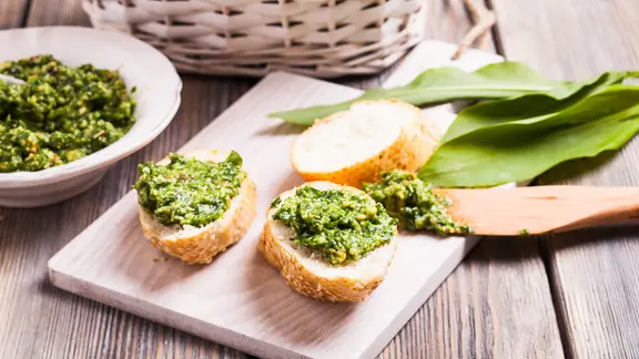 Geschnitten Brotscheiben mit Bärlauch-Pesto, im Hintergrund einige Blätter Bärlauch.