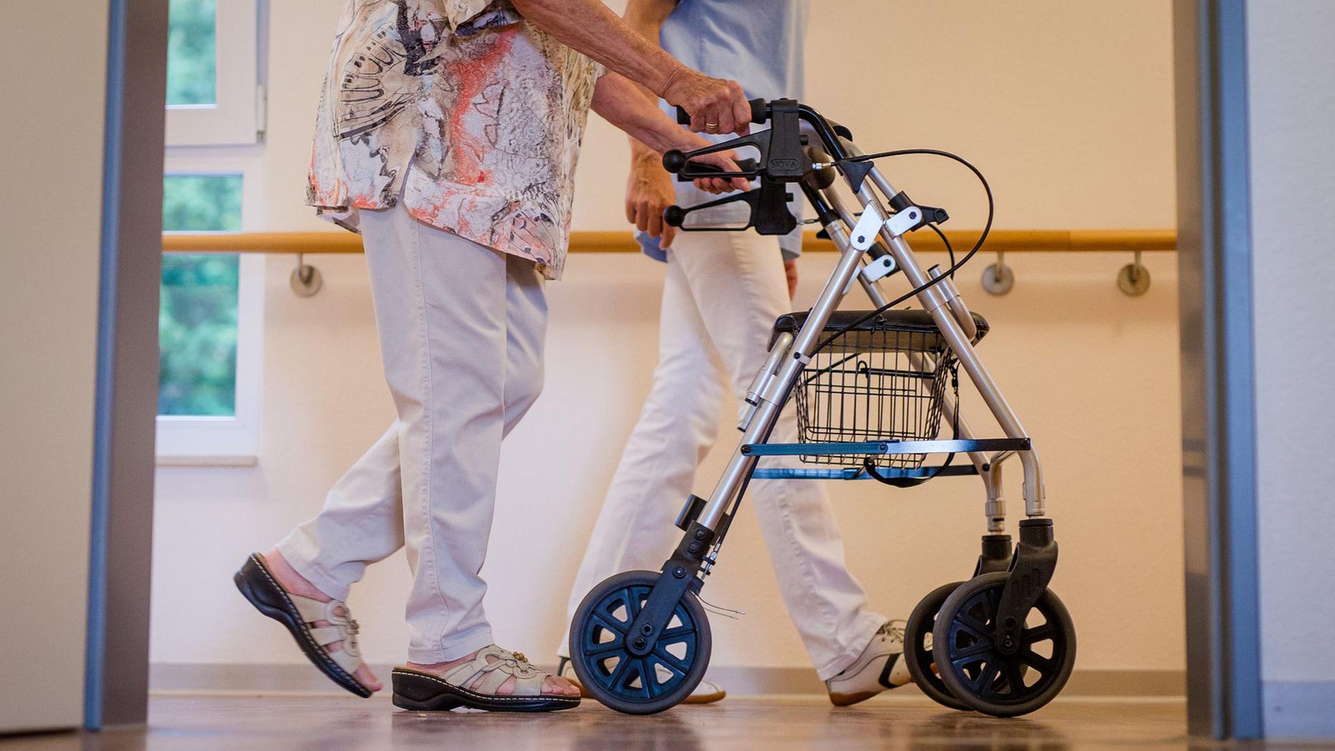 Eine Pflegekraft begleitet eine älteren Dame über den Korridor eines Pflegeheims | Christoph Schmidt