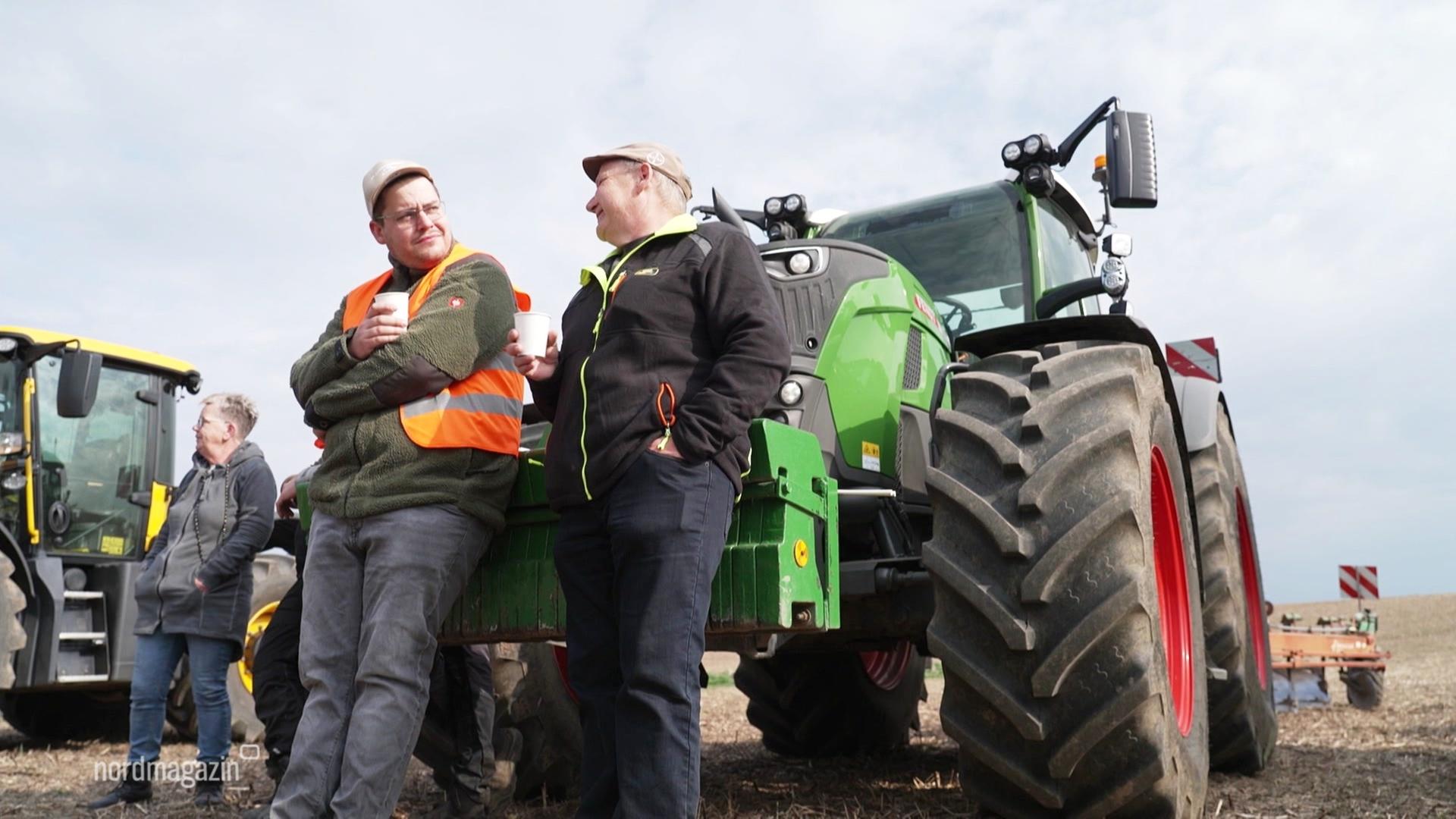 Zwei Landwirte stehen vor einem Traktor. | Screenshot