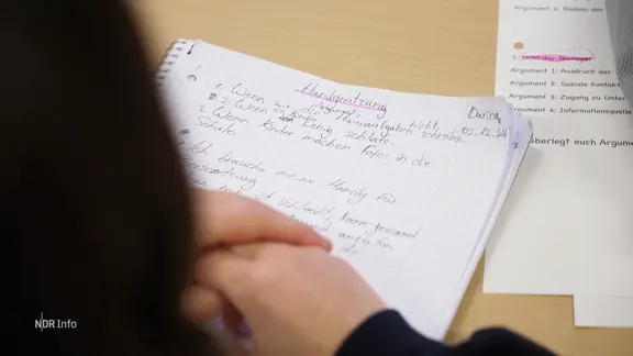 Eine Schülerin notiert in ihrem Colleblock Argumente für und gegen ein Handyverbot.