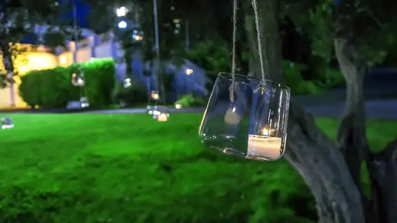 Eine brennende Kerze im Glas hängt an einem Baum