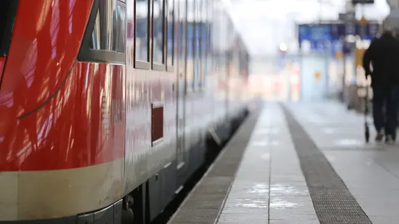 Ein Zug der Regionalbahn steht mit einer Person am Gleis.