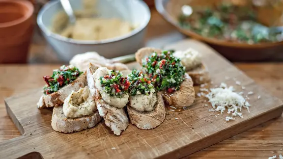 Mit Pastinaken-Creme und Petersilien-Pesto bestrichene Brote auf einem Holzbrett. | NDR, Tarik Rose Mit Pastinaken-Creme und Petersilien-Pesto bestrichene Brote auf einem Holzbrett.