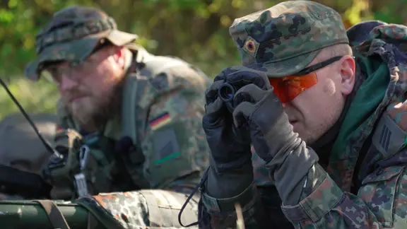 Zwei Soldaten liegen auf dem Boden, einer schaut in ein Fernglas.