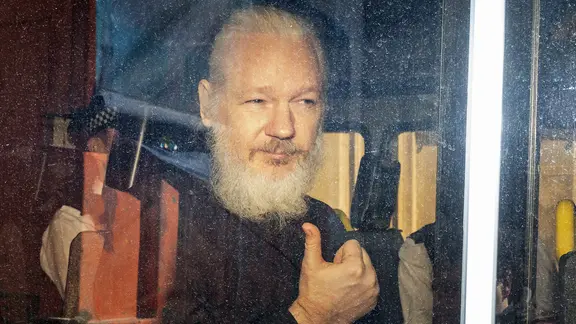 Wikileaks-Gründer Julian Assange sitzt in einem Polizeiauto und schaut aus dem Seitenfenster.