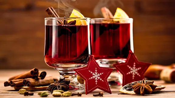 Zwei Gläser mit dampfenden Glühwein, daneben Weihnachtsdekoration.