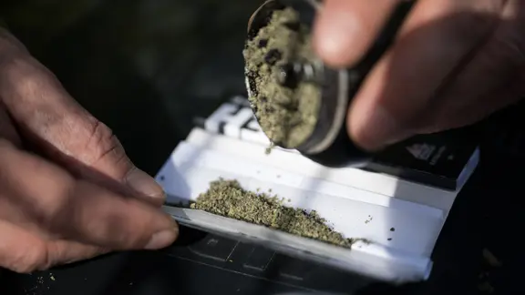 Ein Mann schüttet zerstoßenes Marihuana in einen Joint. 