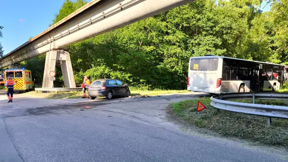 Nach einem Unfall stehen ein Auto und ein Schulbus sowie ein Rettungsfahrzeug unter einer Brücke.