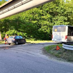 Nach einem Unfall stehen ein Auto und ein Schulbus sowie ein Rettungsfahrzeug unter einer Brücke.