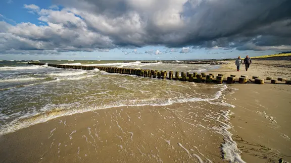 Zwei Menschen spazieren an einem stürmischen Tag am Ostseestrand in Ahrenshoop.