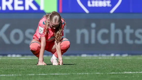 Eine Spielerin hockt auf dem Rasen.