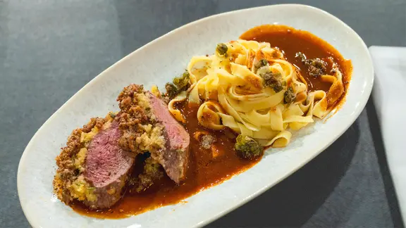 Rehrücken mit Panko-Parmesankruste, Tagliatelle und Soße auf einem Teller angerichtet.