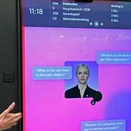 HVV-Chefin Anna-Theresa Korbutt zeigt auf einem Pressetermin auf der Mobilitätsmesse "UITP-Summit" auf einen Bildschirm, der KI-gestützt Fragen von Fahrgästen beantworten soll.