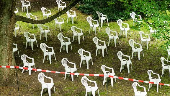 Des chaises en plastique blanc alignées sur une pelouse verte.
