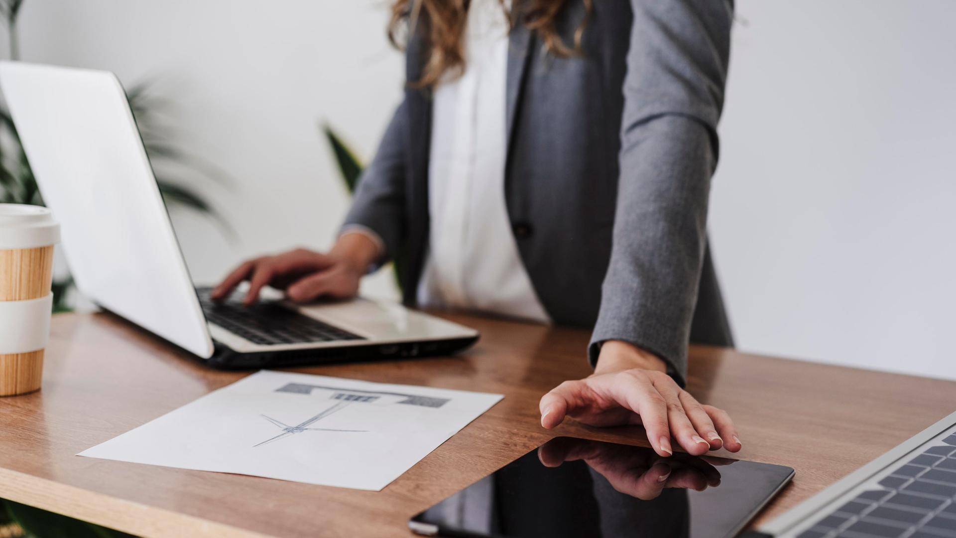 Eine Frau steht an einem Schreibtisch, darauf liegen elektronische Geräte. | picture alliance / Westend61, Eva Blanco