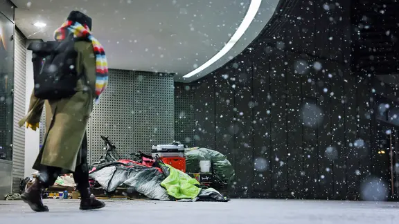 Eine Frau läuft im Schneegestöber in Hamburg an einem Obdachlosen vorbei.