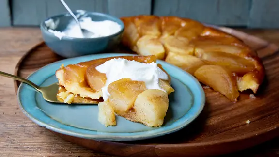 Ein Stück Tarte Tatin mit Schlagsahne auf einem Teller serviert.