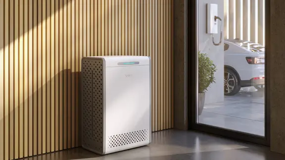 Ein Batteriepsiecher steht in einem Raum, durch das Fenster sieht man ein ladendes E-Auto.