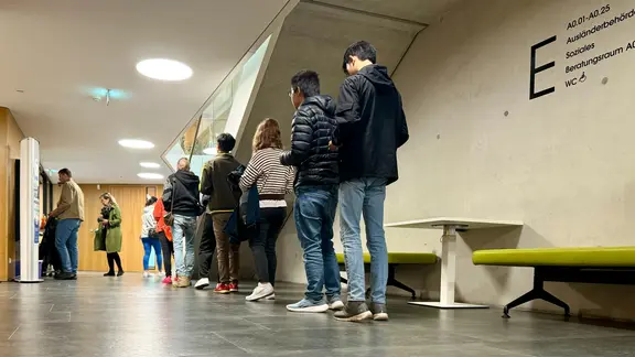 In der Ausländerbehörde in Wismar stehen Menschen auf einem Flur in einer Warteschlange.
