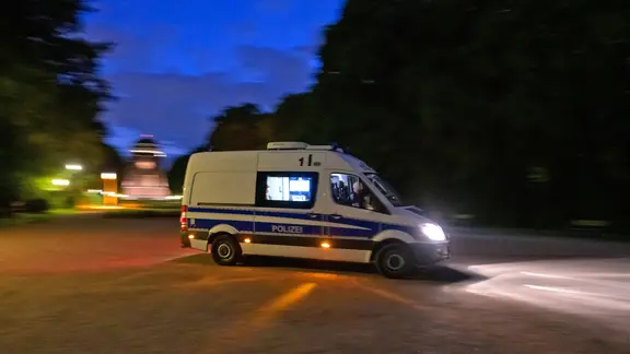 Ein Polizeifahrzeug fährt durch den dunklen, fast menschenleeren Stadtpark vor dem Planetarium.
