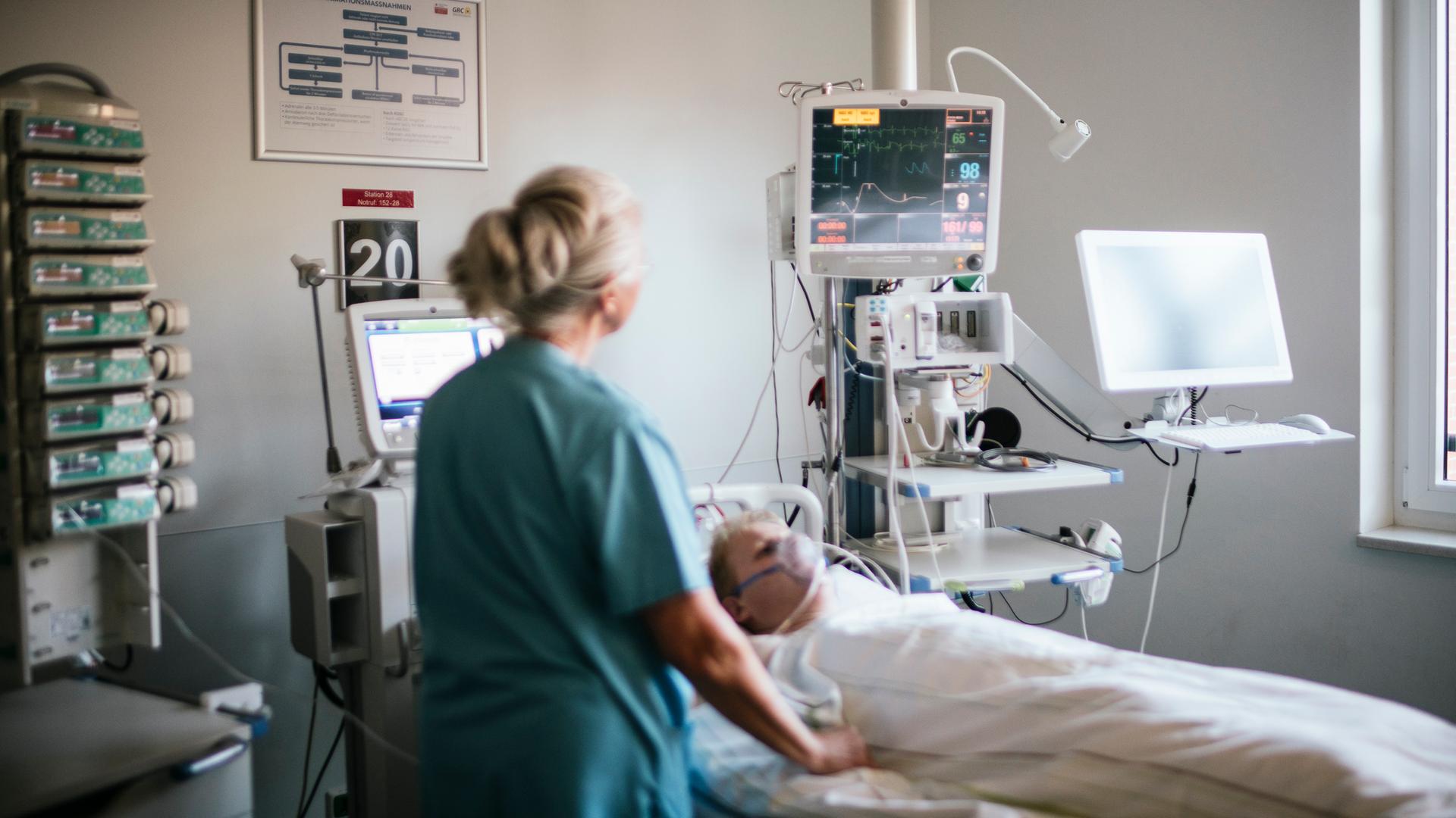 Eine Krankenschwester steht neben einem Patientenbett und schaut auf sein EKG. | NDR, Julius Matuschik