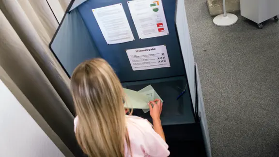 女性は「einer Wahlkabine」で「einen Stimzettel」を読んでいます。