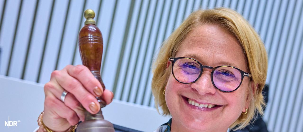 Eine Frau hält lächelnd eine Glocke in die Kamera