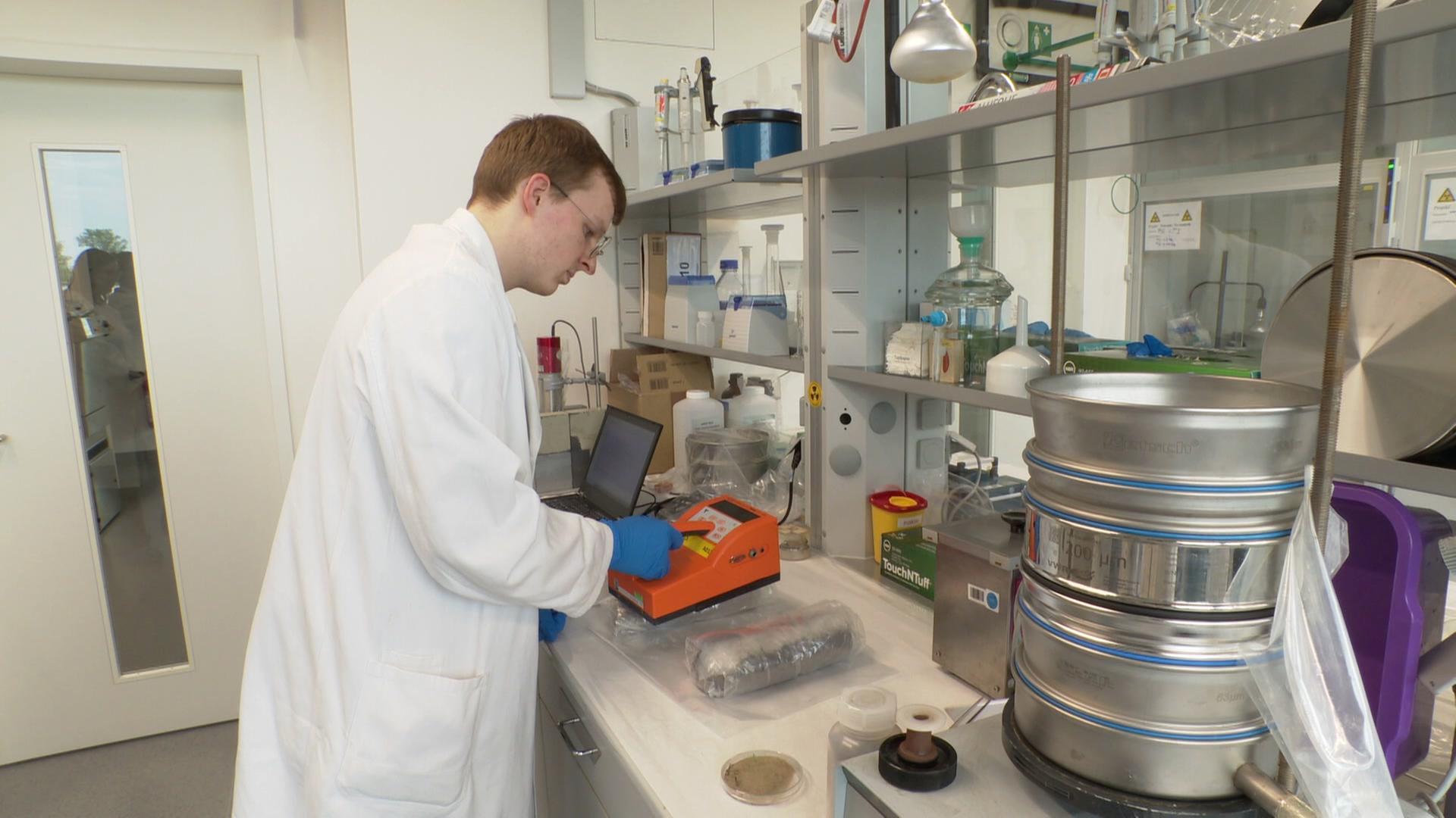 Ein Forscher untersucht Erde in einem Labor. | NDR