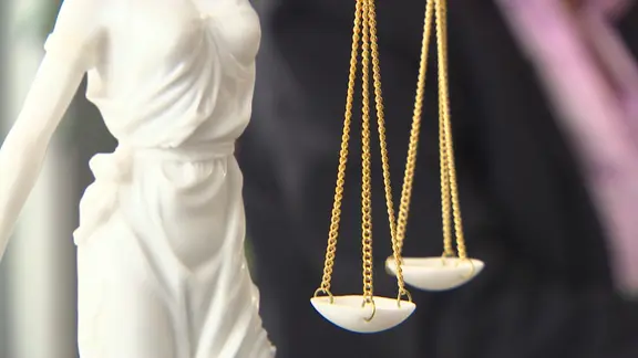 Eine weiße Justitia-Plastik (Göttin der Gerechtigkeit) mit zwei Waagschalen an goldenen Kettchen in Nahaufnahme