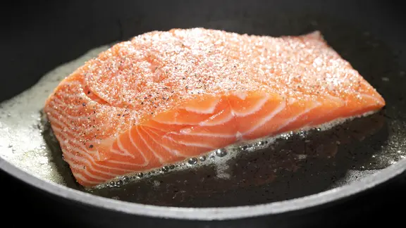 Ein Stück Lachsfilet brät in einer gusseisernen Pfanne.