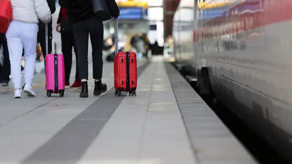 Zwei Frauen mit Koffer von hinten, die am Bahngleis neben einem stehenden ICE entlang gehen