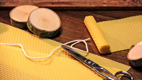 Bienenwachs, ein Docht und eine Schere liegen auf einem Tisch.