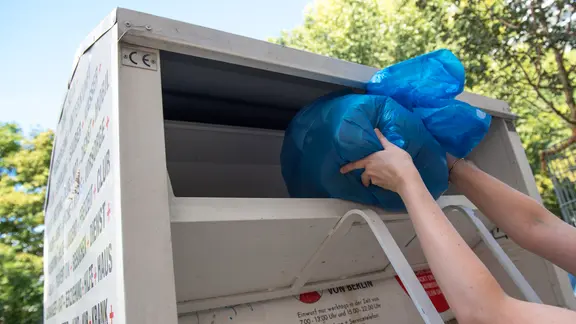 Jemand wirft einen Sack mit Altkleidern in den Altkleidercontainer.