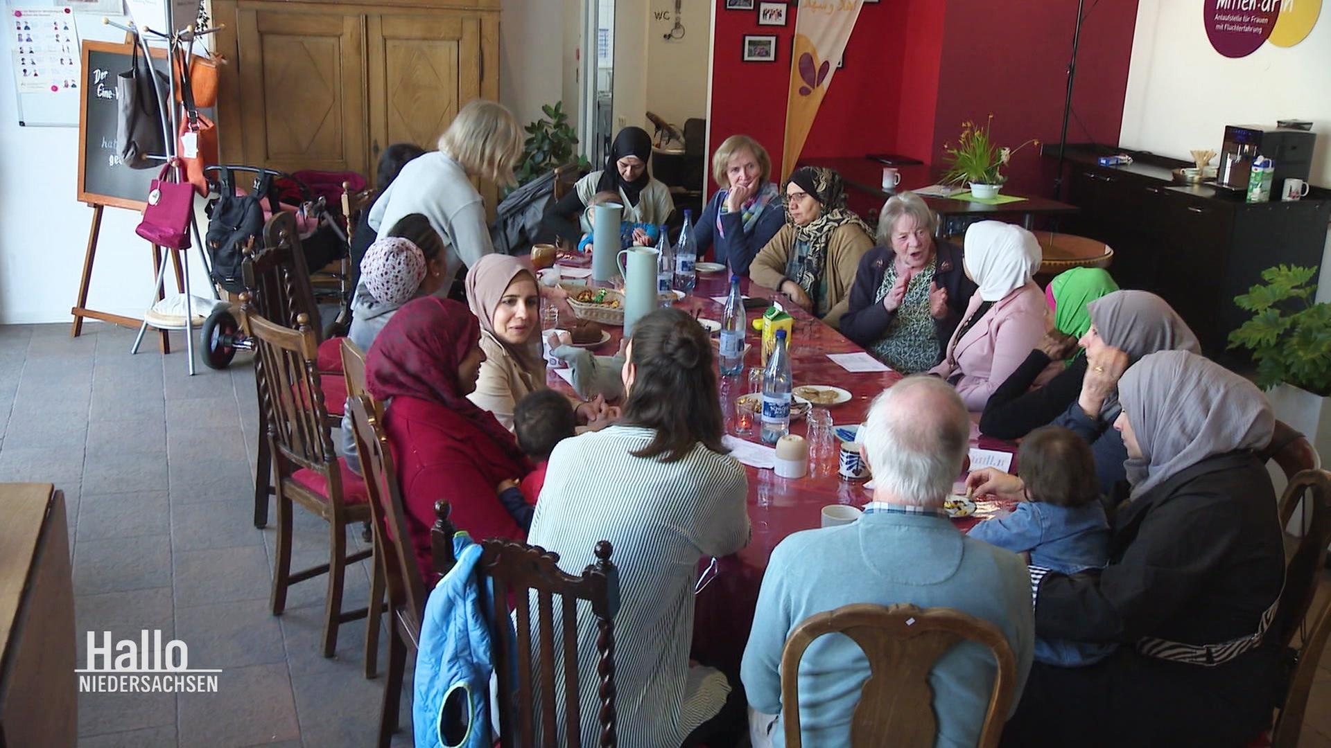 Frauen und Kinder sitzen in einem Café zusammen an einem Tisch. | Screenshot