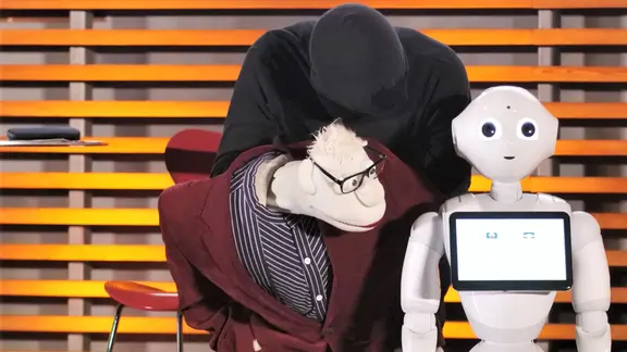 Pepper snackt Platt: Eine Handpuppe (Werner Momsen) und Roboter Pepper auf einer Bühne.